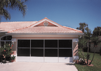 Suburban house with pink roof and screened garage door, surrounded by palm trees and lawn