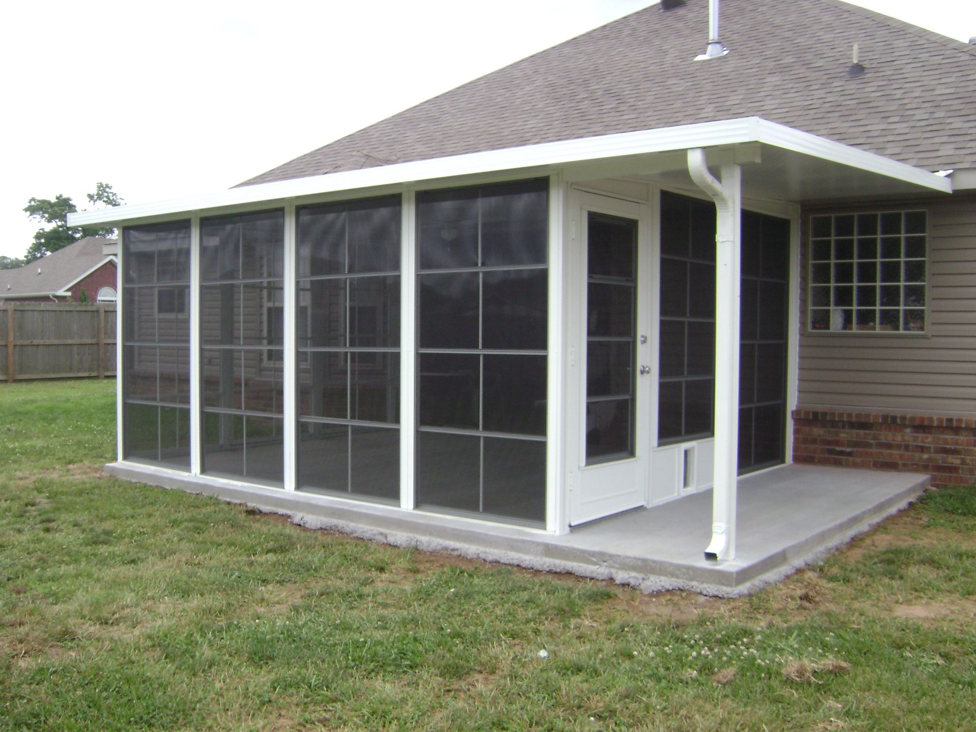 Screened porch enclosure attached to a house with white framing and a gray roof