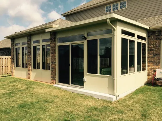 Sunroom addition with cream siding and large windows attached to a house, overlooking a grassy yard
