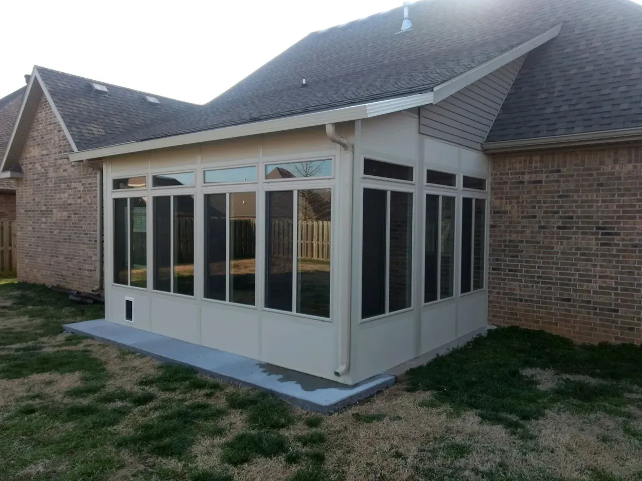 Brick house with a white sunroom extension and multiple windows in a grassy yard.
