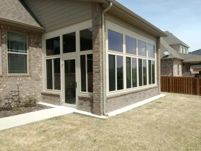 Backyard patio with large screened windows and stone exterior beside a fenced lawn