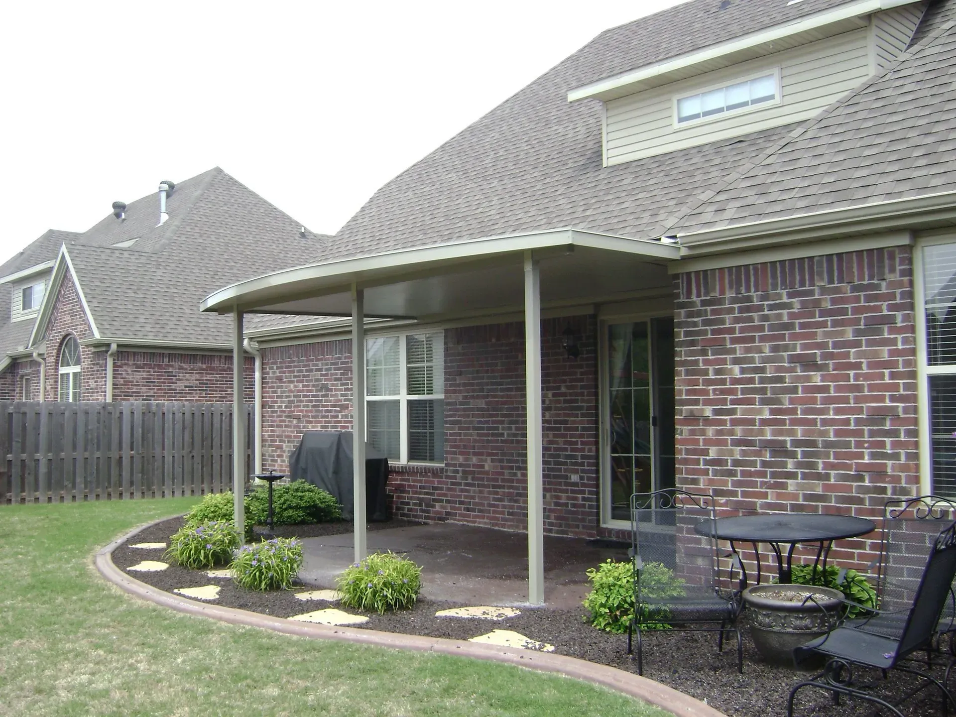 Brick house patio with covered porch, potted plants, and patio furniture in a suburban backyard.