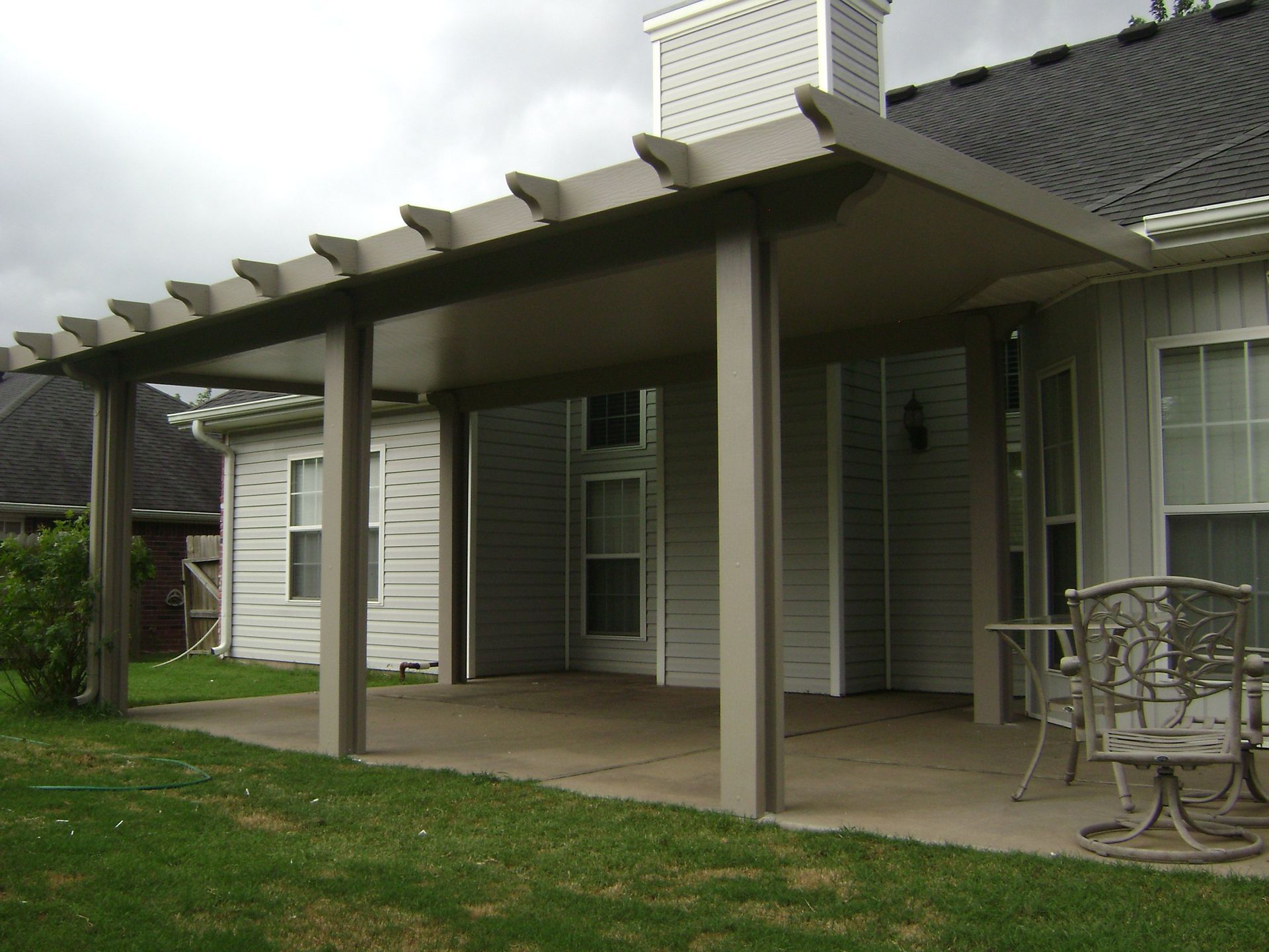 Covered patio with white pergola posts, sliding glass doors, and a metal table on a grassy lawn