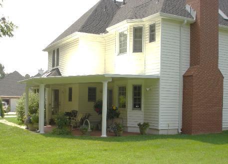 Two-story white house with red brick chimney, porch, and green lawn