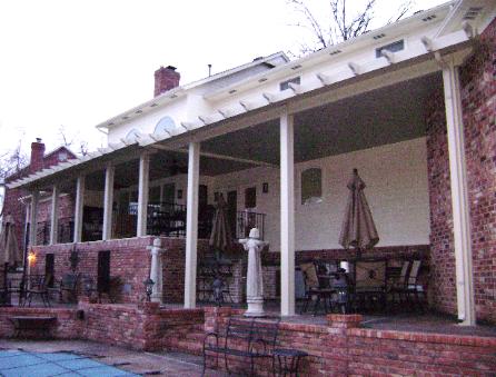Brick house porch with white columns, patio furniture, and a covered walkway outside.