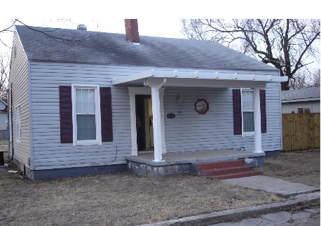 Small white house with a front porch, red steps, and bare winter yard.