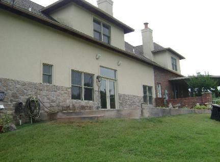 House exterior with stone lower walls, green lawn, and a covered patio under an overcast sky