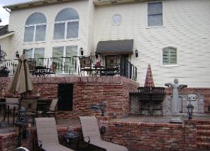 Brick patio with tiered seating, tables, umbrellas, and a white house in the background