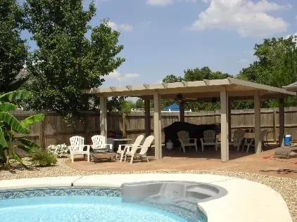 Backyard pool with a white cabana, patio chairs, and trees under a blue sky