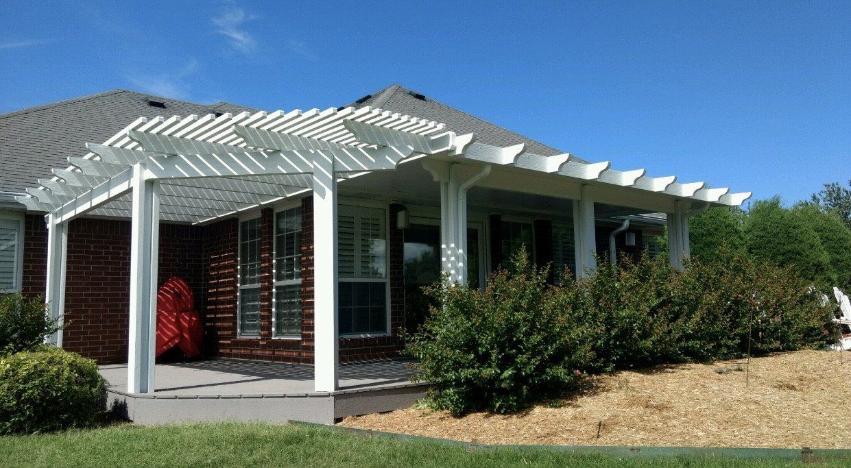 White house with a covered porch, red front door, and trimmed bushes under a bright blue sky