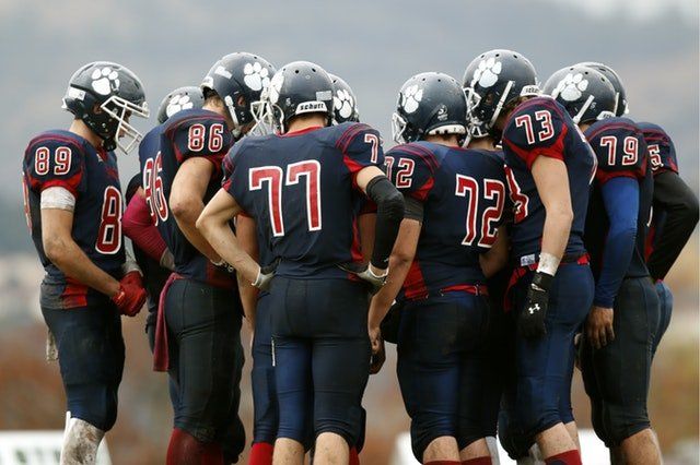 Football team huddle, wearing blue and red uniforms, helmets with paw logo.