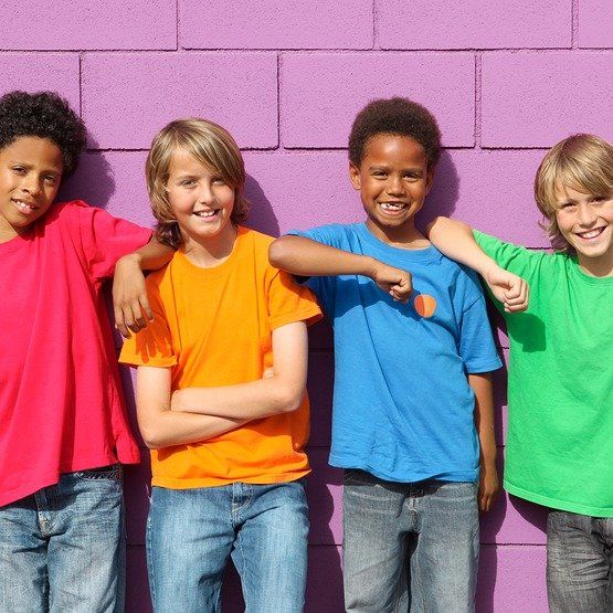 Four children in brightly colored shirts, smiling, leaning against a purple brick wall.