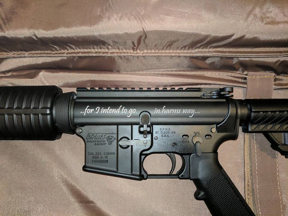 Black AR-15 rifle with engraved text in a brown case.