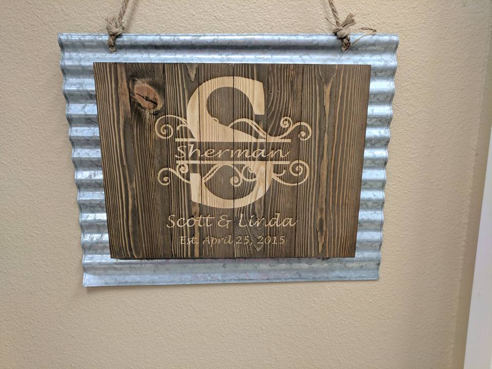 Wooden wedding sign with a personalized monogram and names, set in a corrugated metal frame.