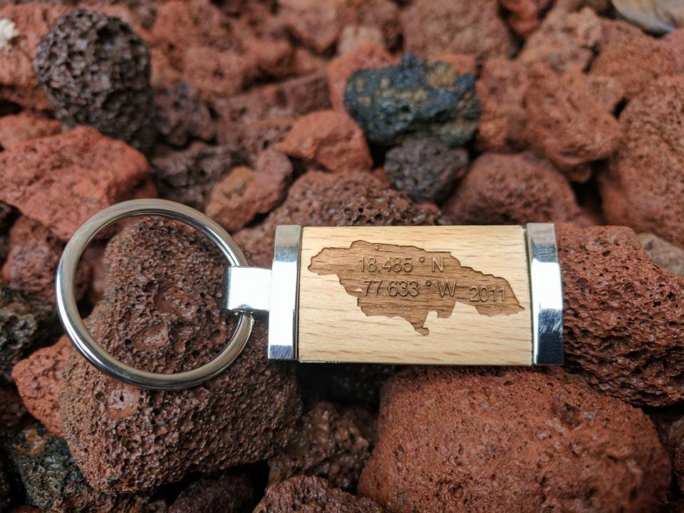 Key chain with Jamaica map etched on wood, set on red volcanic rocks.