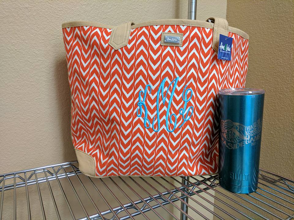 Orange chevron tote bag with blue monogram and teal tumbler on a shelf.