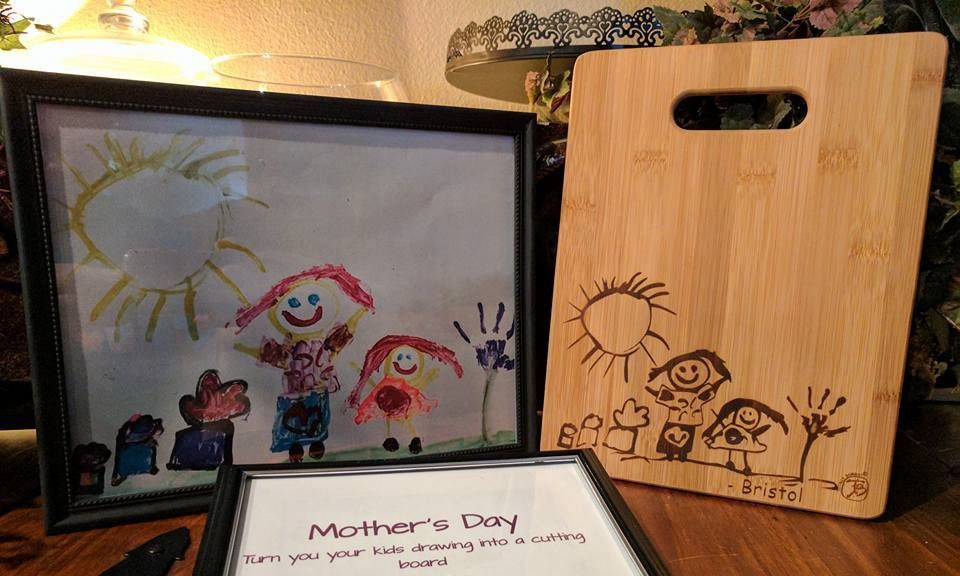 Child's drawing framed next to a wood cutting board etched with a similar design. Mother's Day card below.