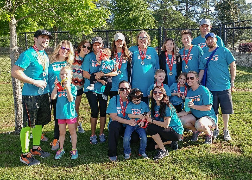 Group of people in teal shirts and medals pose outside.