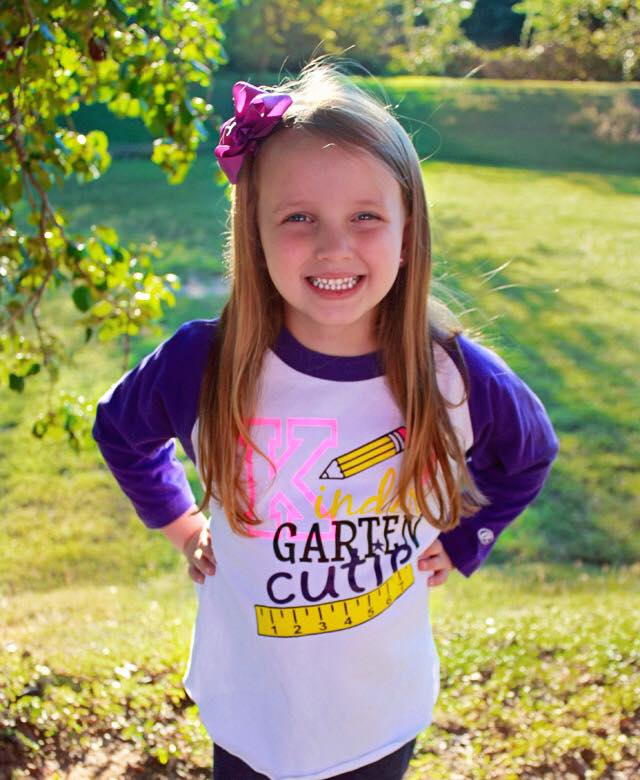 Girl with a purple bow smiles, wearing a