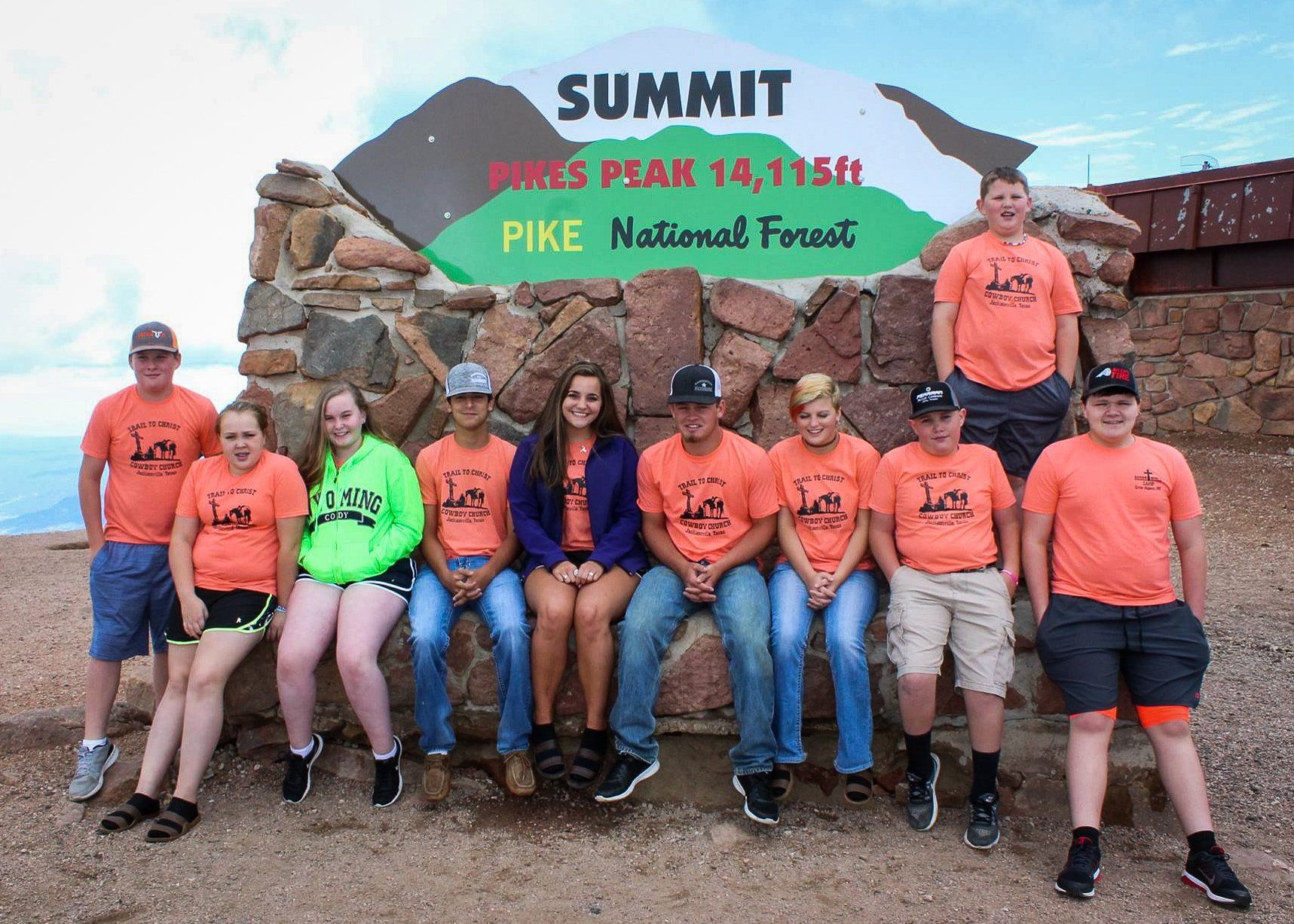 Group of people in orange shirts at the Pikes Peak summit sign.