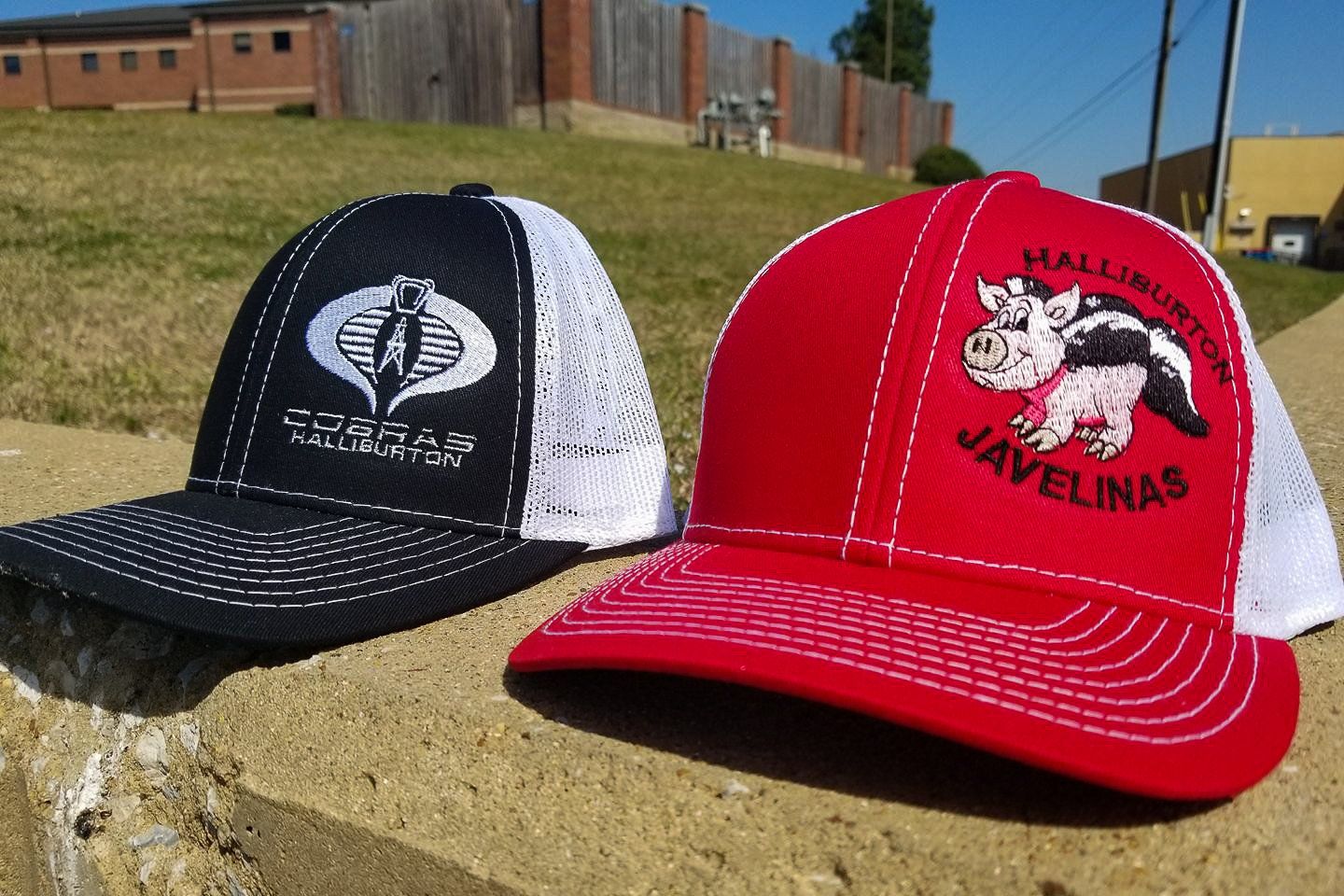 Two trucker hats: one black with a white Cobra logo, and one red with a pig logo, outside.