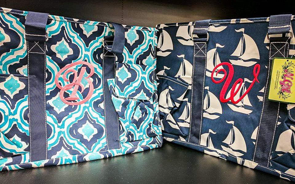 Two tote bags with monograms, one blue ikat pattern, one navy sailboat pattern.