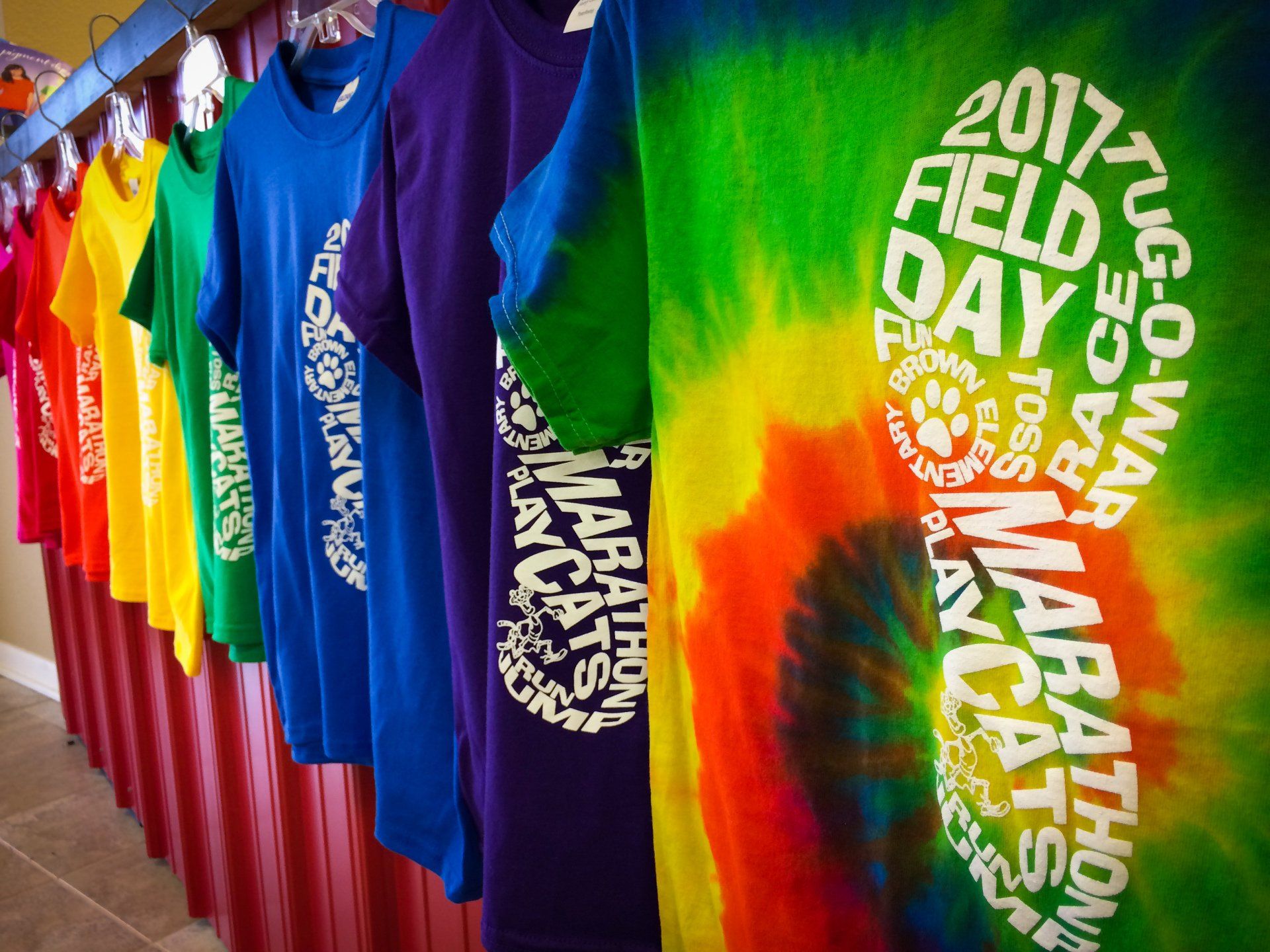 Colorful t-shirts on hangers. The shirts are in a row, including tie-dye. Text on shirts mentions 