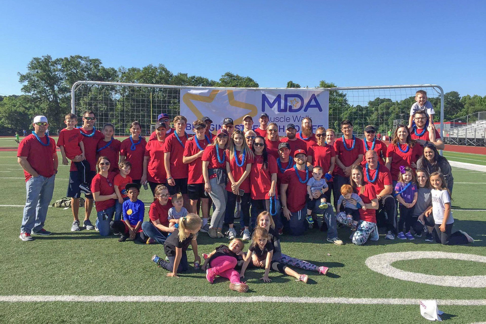 Group of people in red shirts pose on a football field with an MDA banner.