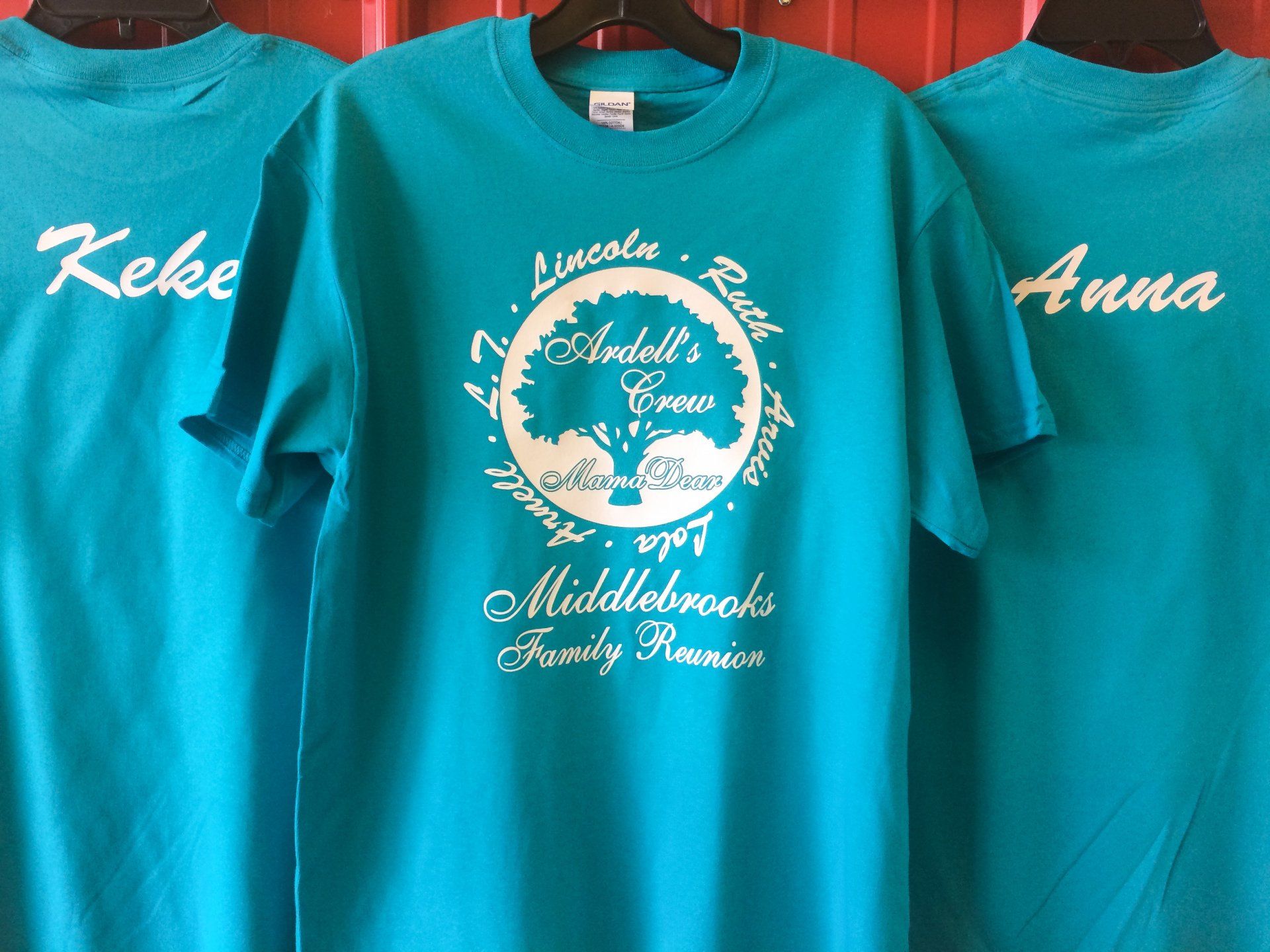 Three turquoise t-shirts with white lettering. One displays 