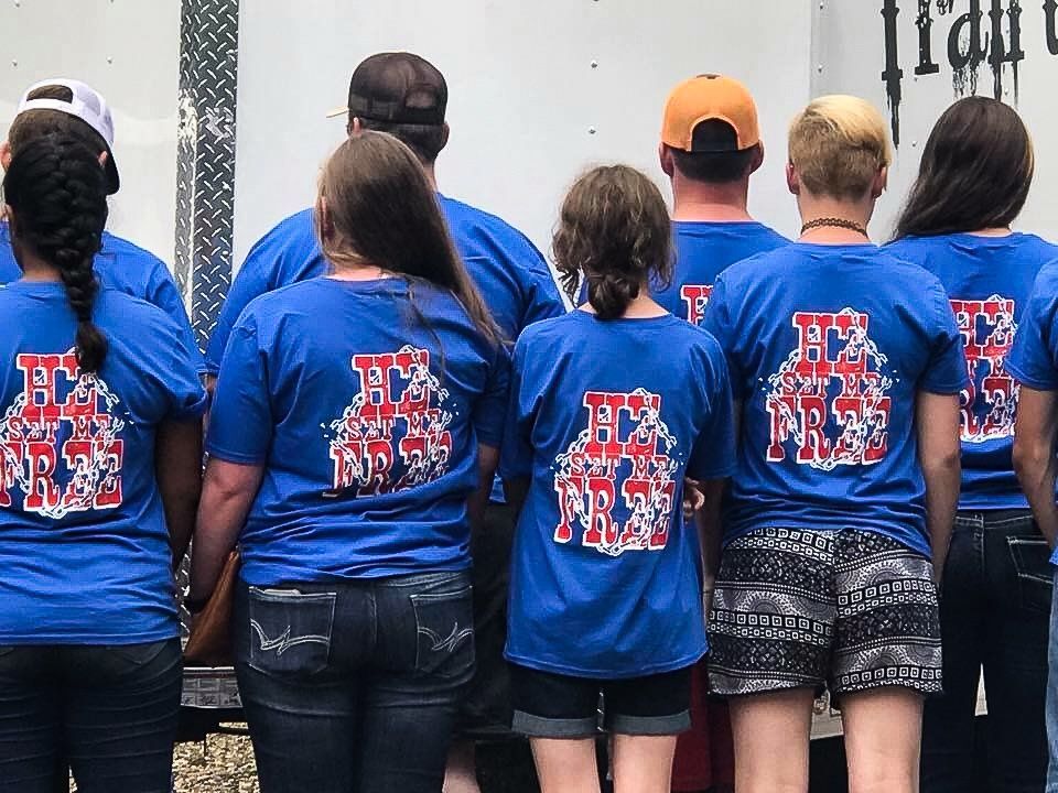 People in blue shirts with a graphic, standing outdoors. The shirts display