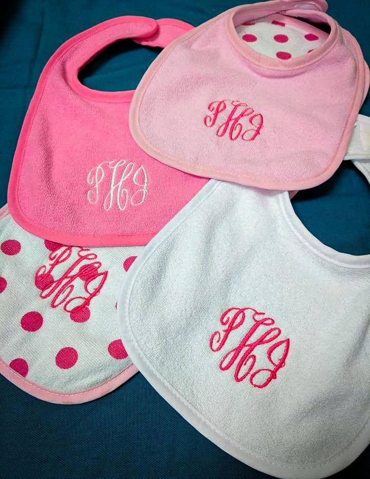 Four pink and white baby bibs with embroidered initials.
