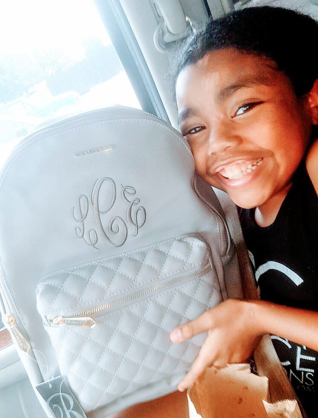 Smiling person with new gray backpack; monogram and quilted pocket detail.