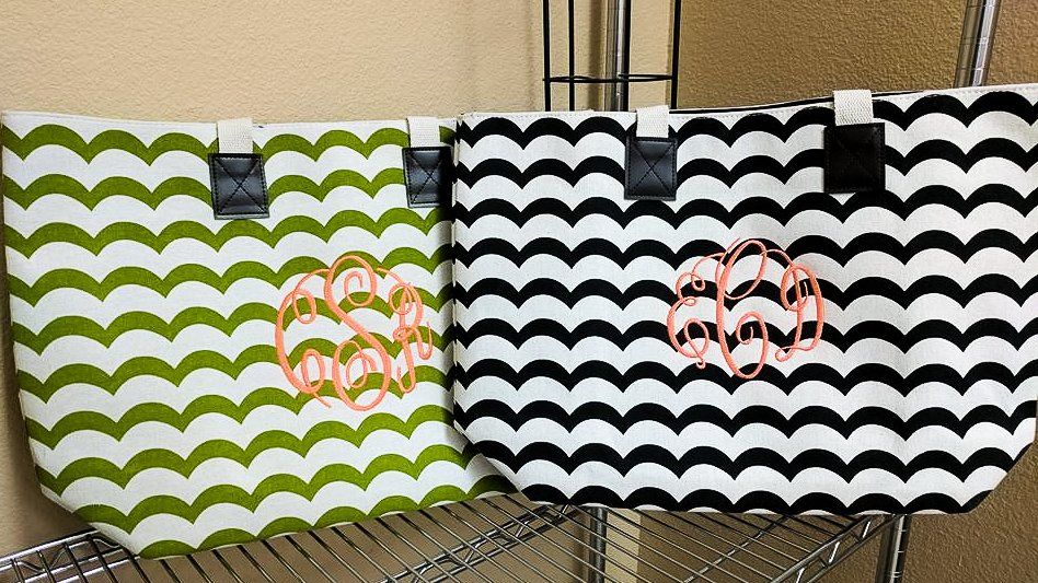 Two patterned tote bags: green and white, and black and white, with pink monograms, on a shelf.