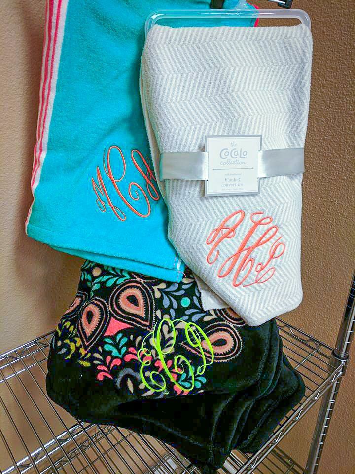 Three personalized towels: teal, white, and black with floral pattern, each embroidered with initials.