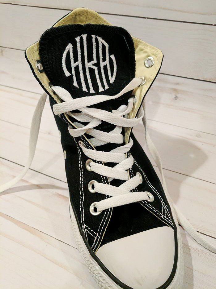 Black Converse high-top sneaker with white laces and a monogram embroidered on the tongue.