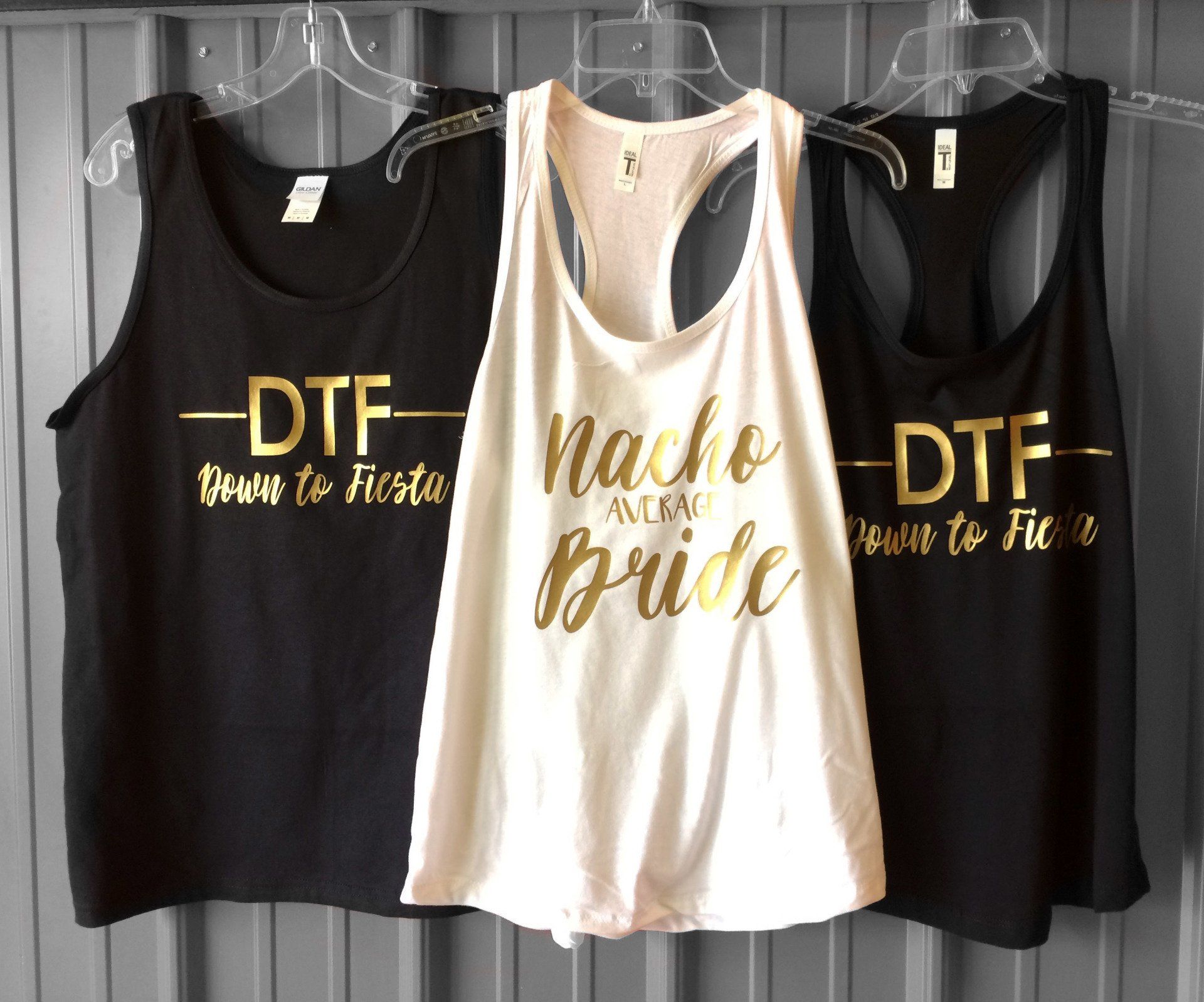 Three tank tops hanging; black with gold text