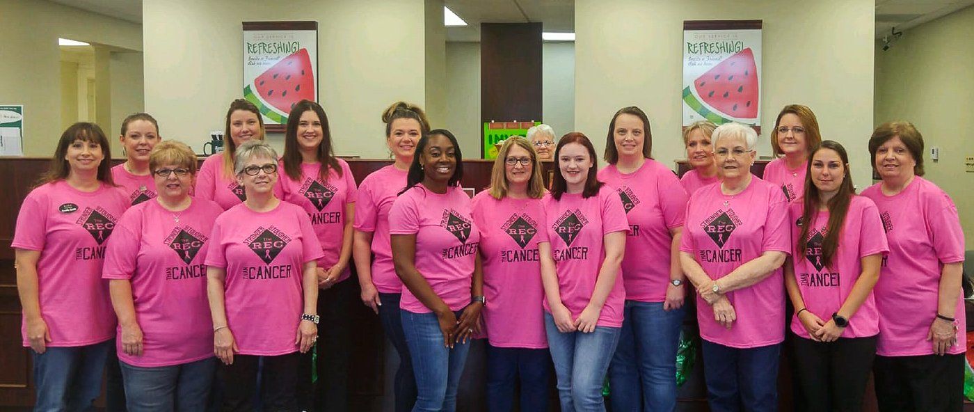 A group of women in pink shirts standing together indoors, some smiling.