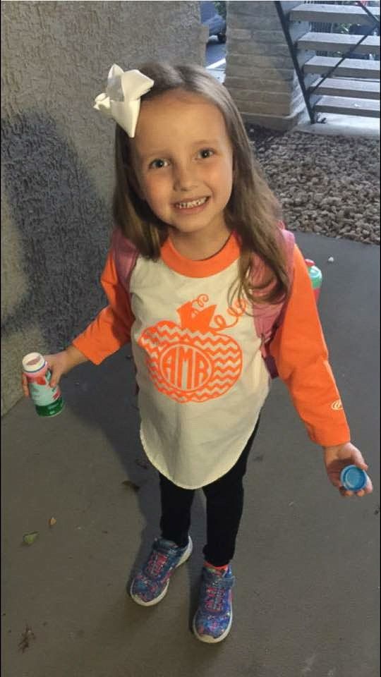 Girl smiling, holding bubbles, wearing orange and white shirt, black pants, and a white bow.