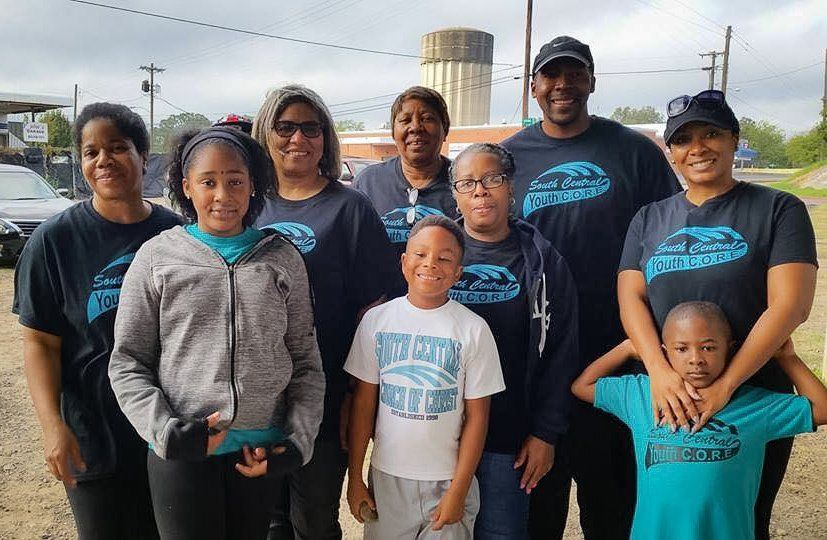 Group of people in matching shirts, smiling outside. Water tower in background.