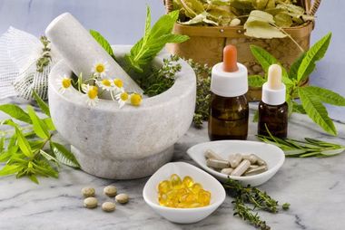 A mortar and pestle surrounded by herbs and pills on a table.