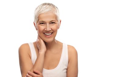 A woman with short gray hair is smiling and touching her face.