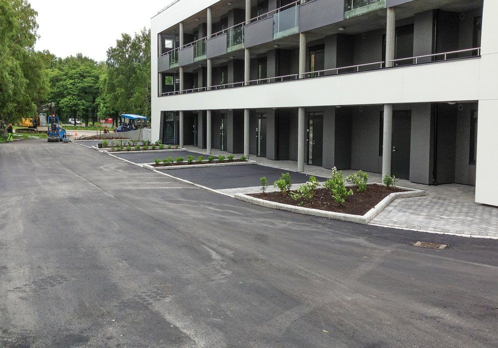 Asfaltert uteområde med plantebed og gangfelt foran leilighetsbygg.