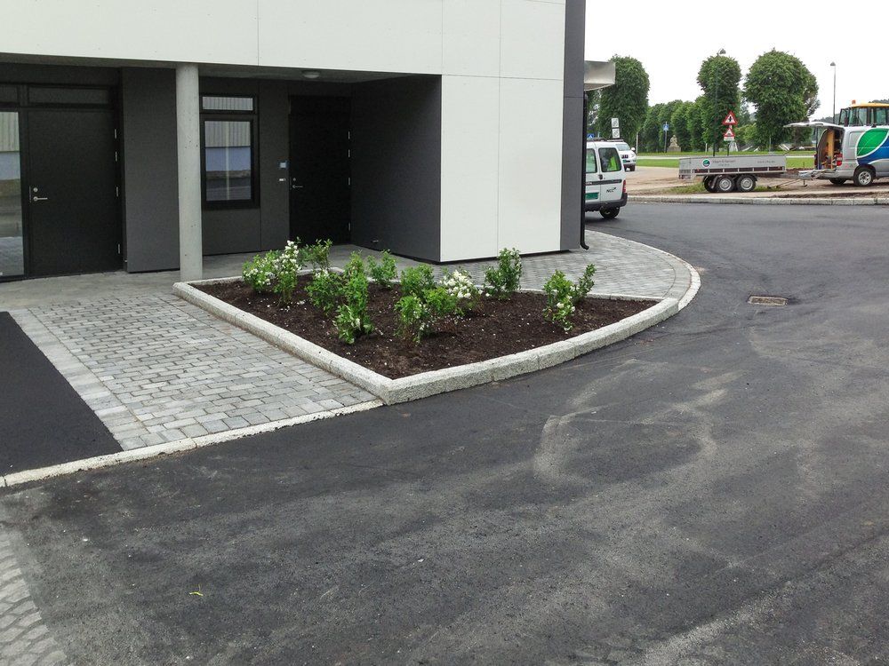 Brosteinslagt gangvei og plantebed ved leilighetsbygg.
