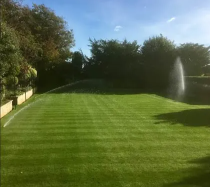 A manicured grass tennis court with irrigation sprinklers