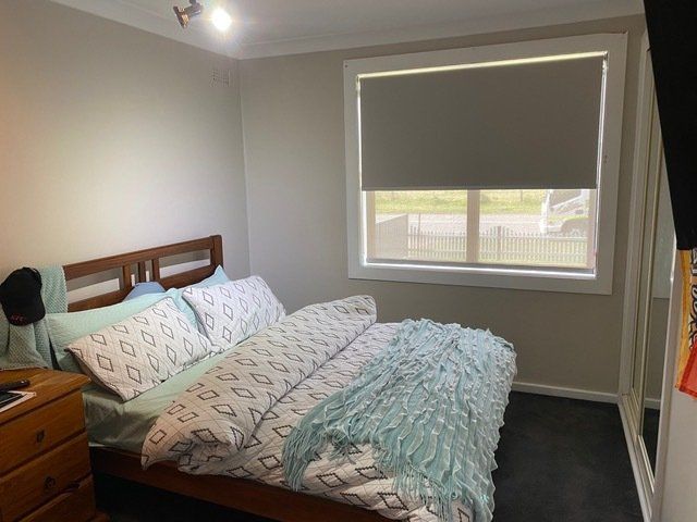 A bedroom with a bed , nightstand , and window — Plantation Shutters in Singleton, NSW
