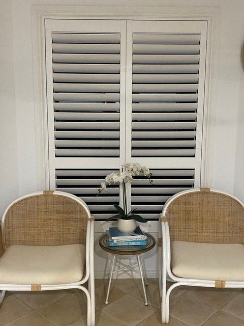 Two chairs are sitting in front of a window with shutters — Plantation Shutters in Singleton, NSW