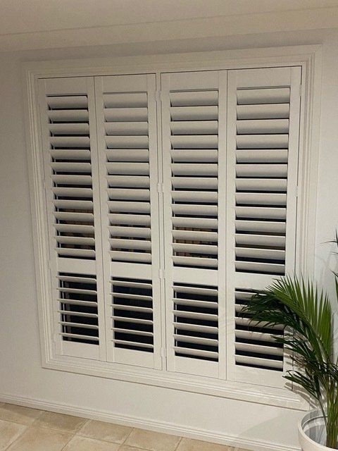 A window with white shutters and a potted plant in front of it — Plantation Shutters in Singleton, NSW