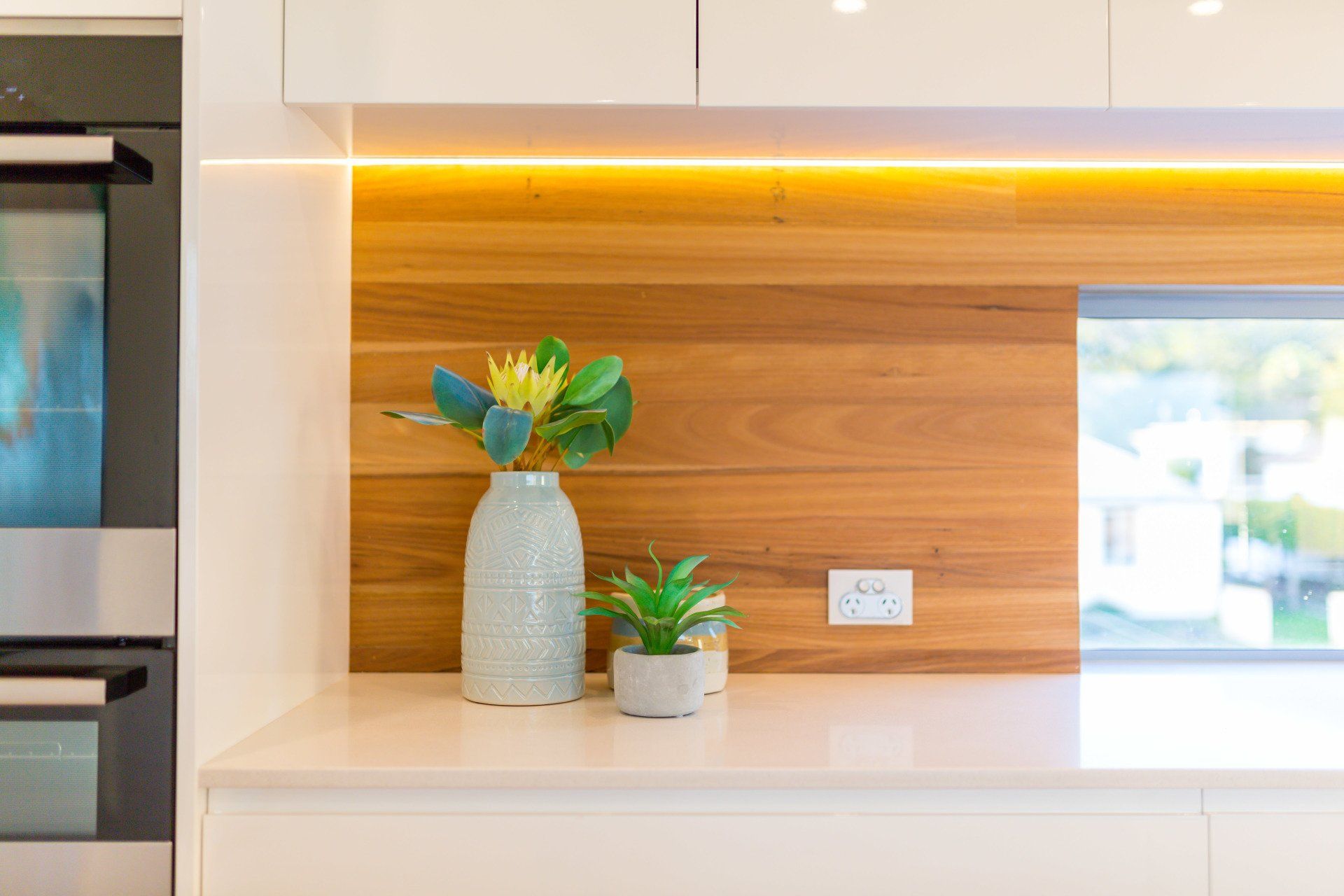 A kitchen counter with a wood backsplash, vase of flowers, and small potted plant.
