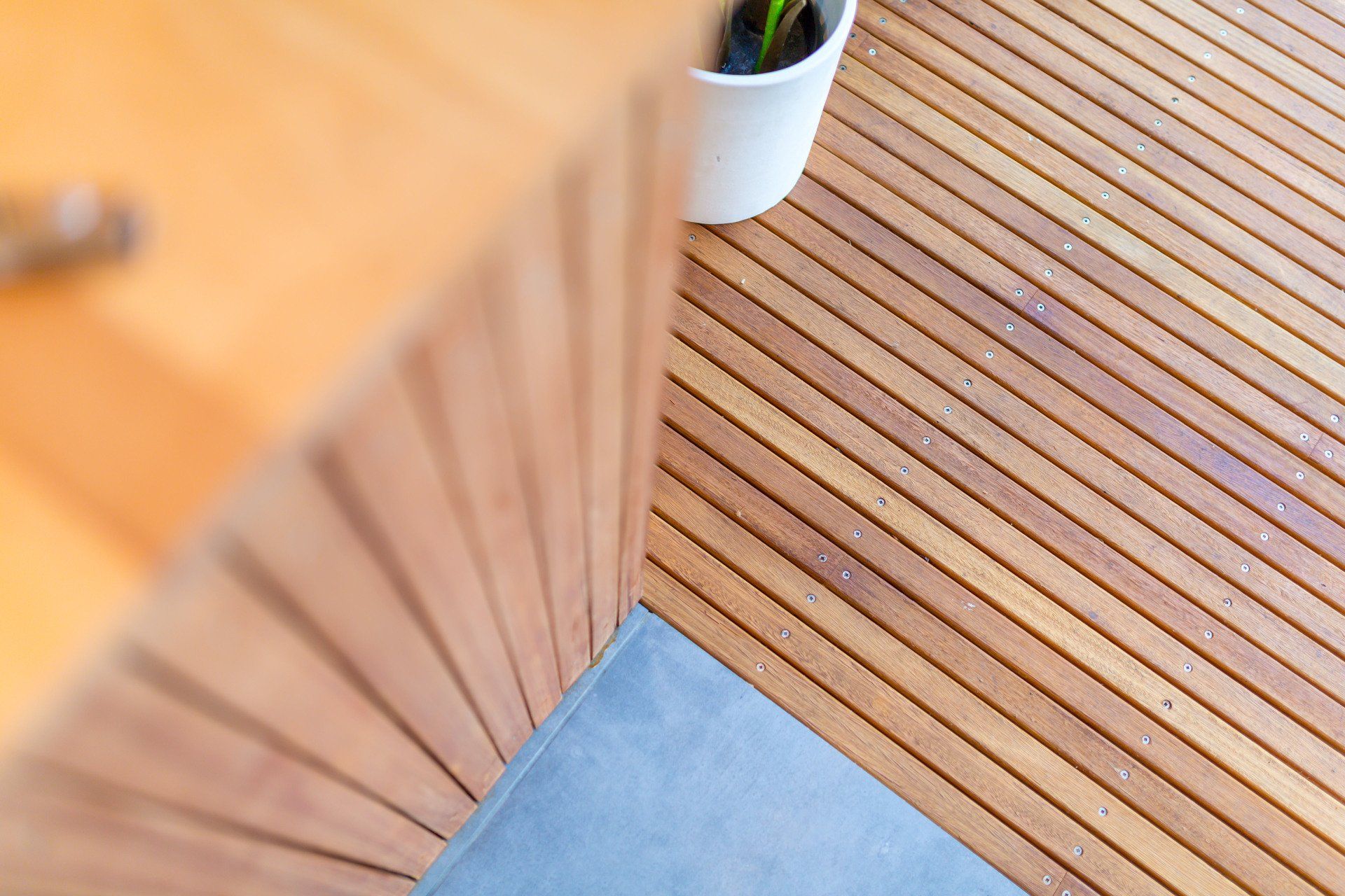 Overhead view of a wood table and deck with a gray corner and a potted plant.