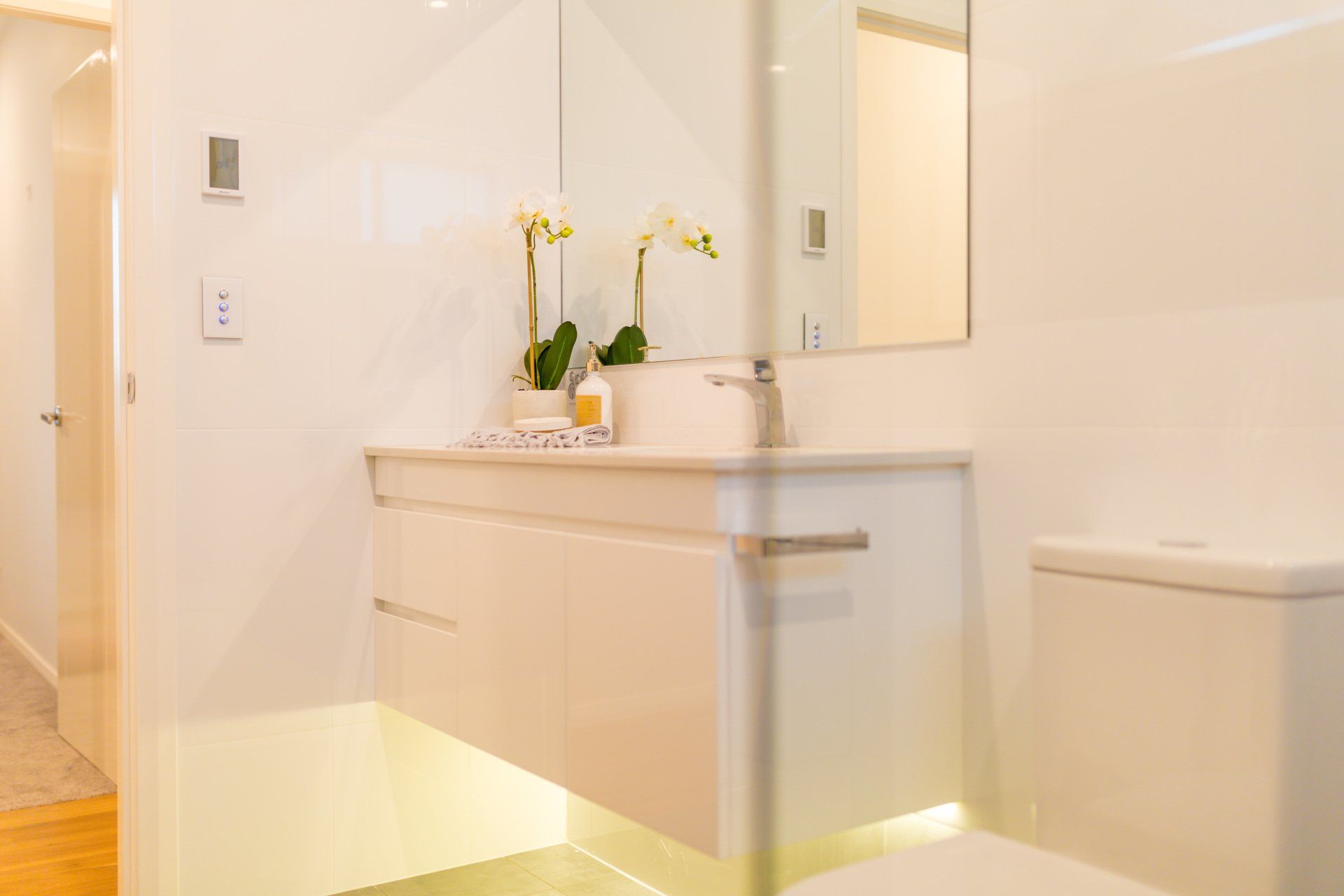 Modern white bathroom with floating vanity, toilet, and mirror.